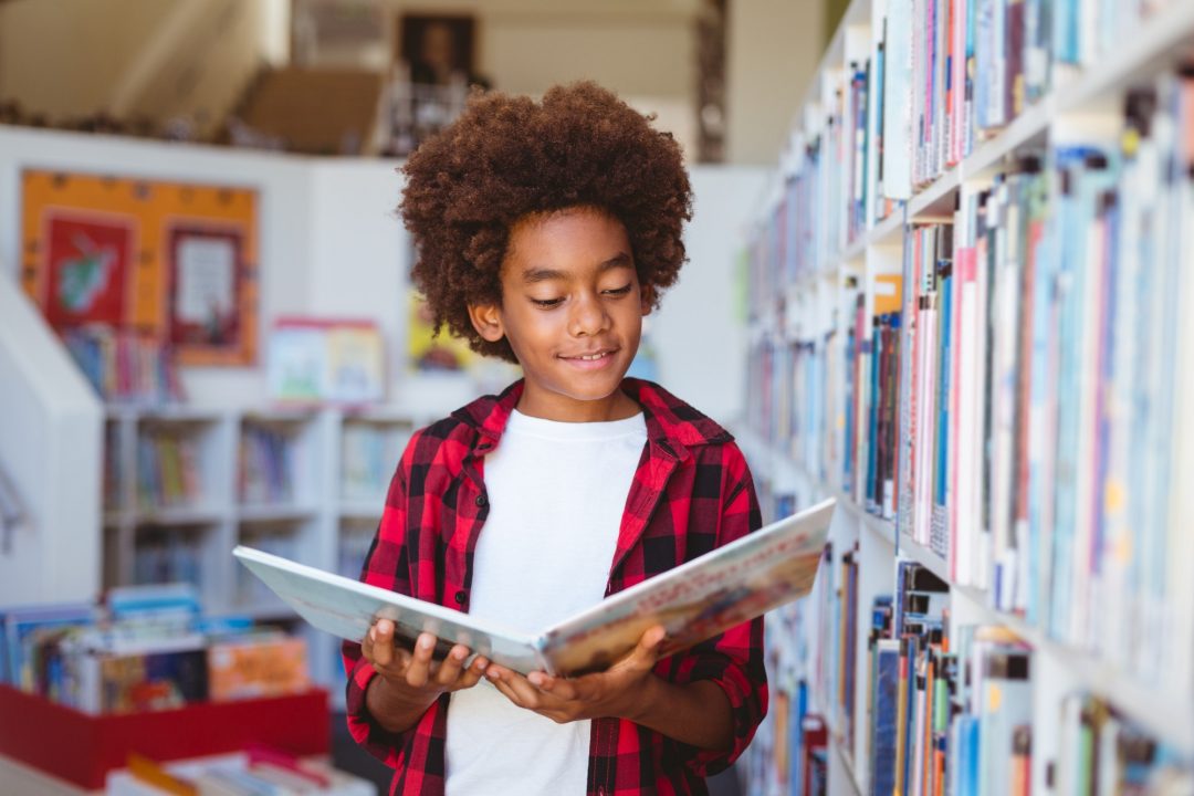 smiling-african-american-schoolboy-reading-book-standing-in-school-library (1)